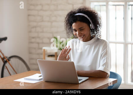 Felice African American business giovane donna che indossa le cuffie, salutando. Foto Stock