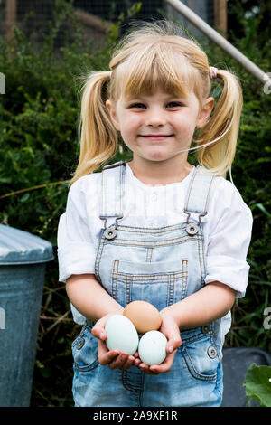 Ragazza bionda in piedi in un giardino, tenendo le uova fresche, sorridente alla fotocamera. Foto Stock