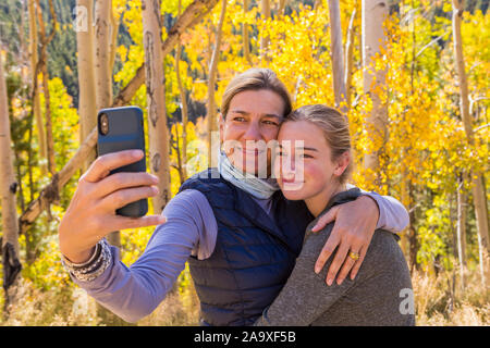 Ritratto di sua madre e la sua 13 anni con la figlia con autunno aspens in background, prendendo un immagine selfie Foto Stock