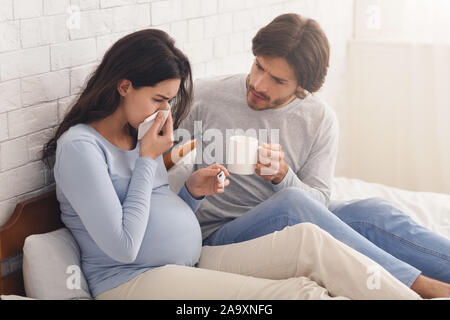 Il marito guardando dopo i suoi malati moglie incinta che soffrono di influenza Foto Stock