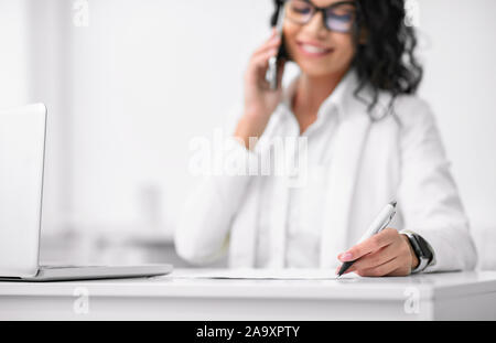Donna latina parlando al telefono e la scrittura Foto Stock