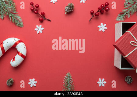 Telaio di Natale fatto di rami di abete, bacche rosse, i fiocchi di neve, candy cane, confezione regalo e pigne su sfondo rosso. Sfondo di natale. Lay piatto. Foto Stock