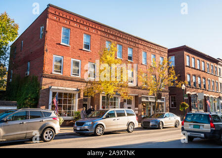 Americane tradizionali edifici in mattoni con negozi lungo una strada trafficata al tramonto. Woodstock, VT, Stati Uniti d'America. Foto Stock