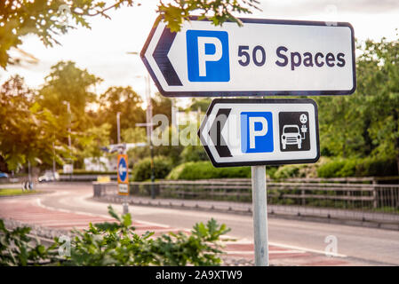 Segnaletica direzionale lungo una strada indicaticating un parcheggio con una stazione caricabatterie per i veicoli elettrici Foto Stock