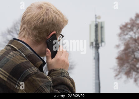 Hemmingen, Germania. Xviii Nov, 2019. Illustrazione - un uomo sta chiamando con uno smartphone accanto a una stazione base (telefono cellulare montante) sulla B3 autostrada federale nella regione di Hannover (staged scena). Il governo federale vuole migliorare radicalmente Internet e telefono mobile reception in Germania nel corso dei prossimi due anni. Credito: Julian Stratenschulte/dpa/Alamy Live News Foto Stock