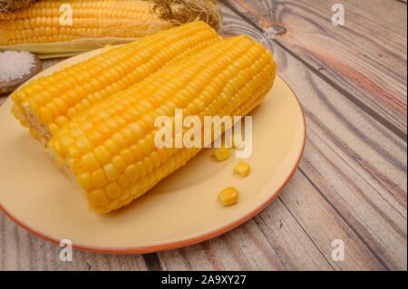 Due bollito di spighe di grano su una piastra e materie spighe di grano su un tavolo di legno. Dieta sana. Dieta Fitness. Per una dolcezza. Close up Foto Stock