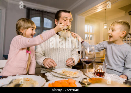 Vecchio bello nonno con i suoi due nipoti seduti al tavolo della cucina e mangiare la pasta. Bambina e ragazzo nonno di alimentazione con pasta Foto Stock