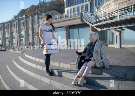 Volunteer sorridere mentre arrivando al pensionato povero in strada Foto Stock