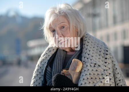 Senzatetto donna Cappotto con sulle spalle tenendo il pane Foto Stock