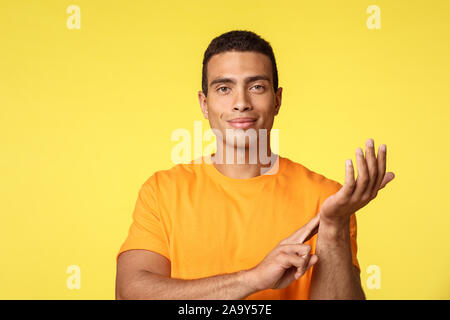 Salute, medicina e concetto di stile di vita. Bello sorridente e fiducioso uomo in giallo t-shirt, misurando il proprio polso, solleva un braccio e toccare vena su Foto Stock