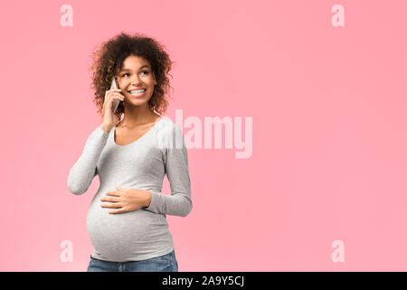 Excited donna incinta parlando sullo smartphone, sfondo rosa Foto Stock