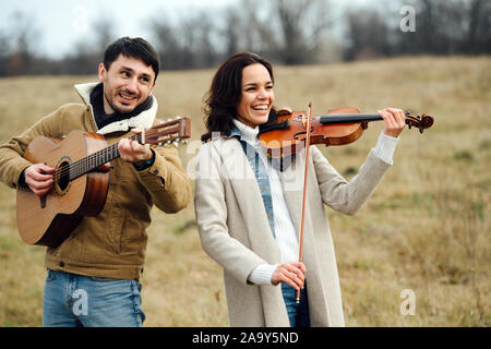 Calorosamente i musicisti vestiti ridere insieme durante la riproduzione in campagna in autunno Foto Stock