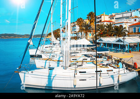 Barche a vela in una splendida e soleggiata baia. Acque turchesi del Mar Egeo sulla costa della città di porto di Poros, Grecia. Vela famosa destinazione di viaggio in Grecia, l'Europa. Uomo Legge giornale. Foto Stock