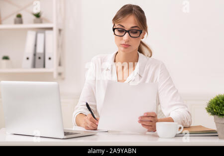 Office lettura della ragazza Business Report prendendo appunti seduti al posto di lavoro Foto Stock