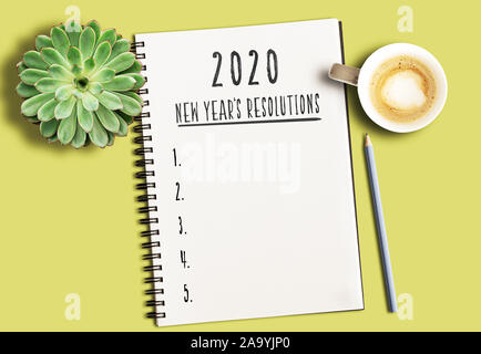 Vista superiore del blocco note con il testo 2020 nuovi anni di risoluzioni e elenco numerato su giallo scrivania con piante succulente e tazza di caffè Foto Stock