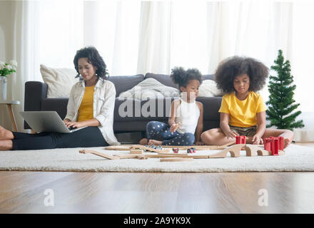 La mamma e i bambini nel soggiorno i bambini giocando insieme di disegno sul pavimento mentre il giovane mamma un momento di relax a casa sul divano, bambina divertendosi Foto Stock