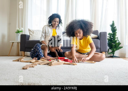 La mamma e i bambini nel soggiorno i bambini giocando insieme di disegno sul pavimento mentre il giovane mamma un momento di relax a casa sul divano, bambina divertendosi Foto Stock