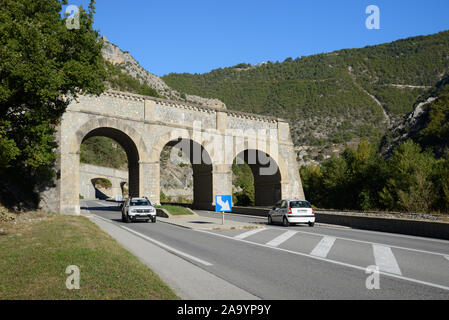 Le automobili guidano sotto una scalla di roccia, un overbridge del canale dell'acqua o un acquedotto progettato per cangere l'acqua del fiume & overspill sopra strada per impedire l'inondazione Francia Foto Stock