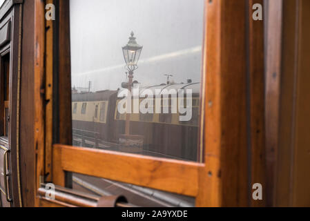 La riflessione della vecchia lampada a gas & treno vintage nella finestra di terza classe, teak vintage carrello ferroviario a fianco di piattaforma a vintage stazione ferroviaria. Foto Stock