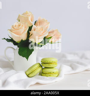 Due verde chiaro macarons francese con tenera Rose in un vaso su sfondo bianco. Close up. Il pistacchio macarons. Posto per il testo. Foto Stock