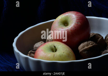 Rosso e giallo kanzi apple con tutta le noci in un bianco coppa di frutta in sfondo blu scuro Foto Stock