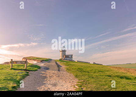 Un faro è appollaiato sul bordo di chalk scogliere di Beachy Head con una bassa sun evidenziando la superficie bianca. Un percorso è in primo piano e Foto Stock