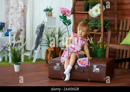 Bambina con un grande fiore seduto su una valigia Foto Stock