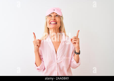 Medioevo donna che indossa la maschera del sonno e pigiama isolato su sfondo bianco meravigliato e sorpreso cercando e dispositivo di puntamento con le dita e ha sollevato il braccio Foto Stock