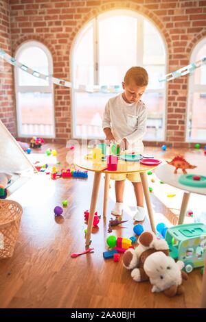 Bella bionda toddler giocando in plastica con cibi e piatti. Piedi intorno un sacco di giocattoli a kindergarten Foto Stock