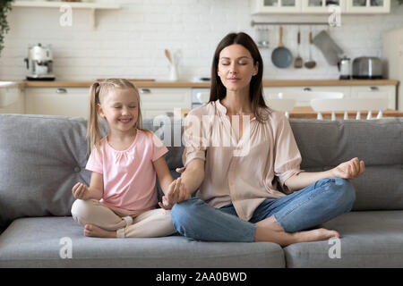 30s donna seduta in lotus posano con incantevole piccola figlia. Foto Stock