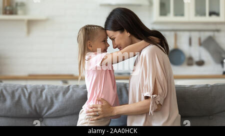 Poco in età prescolare abbracciando la ragazza sorridente giovane mamma, toccando fronte. Foto Stock