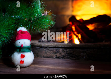 Pupazzo di neve sotto un albero di Natale vicino ad un caminetto, close-up, composizione di Natale Foto Stock