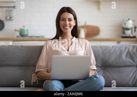 Sorridente imprenditrice seduta su un comodo divano a casa con il computer. Foto Stock