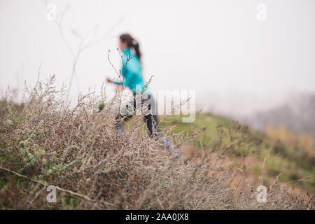 Femmina sportive sale sulla collina in autunno park. Runner figura al di fuori della messa a fuoco. La messa a fuoco in primo piano. Foto Stock