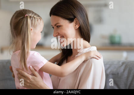 Poco adorabile ragazza di mettere le mani sul sorridente mommys spalle. Foto Stock