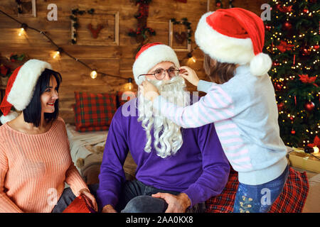 Madre guardando la figlia mettendo Santa barba di padre Foto Stock