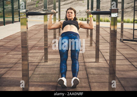 Ragazza treni all'aperto nella palestra di strada. Formazione dei bicipiti e tricipiti. donna barre parallele esercizio di allenamento. atleta femminile esercitando sulle barre parallele Foto Stock