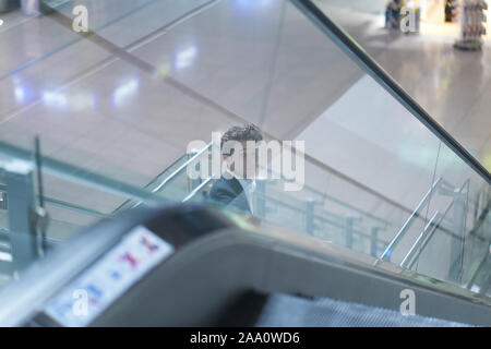 Giovane imprenditore attraente andando verso il basso su una scala mobile in aeroporto, guardando verso l'alto Foto Stock