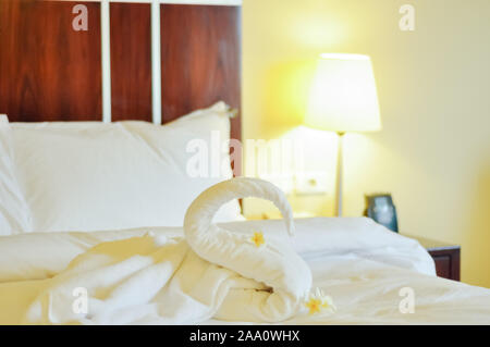 Bellissimo cigno dal bianco asciugamano da bagno decorare sul letto bianco. asciugamano swan con fiori di attualità - frangipani. Bel saluto dall'hotel. Foto Stock