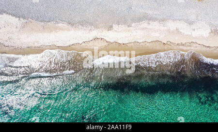 Antenna vista dall'alto in basso con drone di una spiaggia mediterranea con chiare acque blu di sabbia di piccole dimensioni e le onde che si infrangono Foto Stock