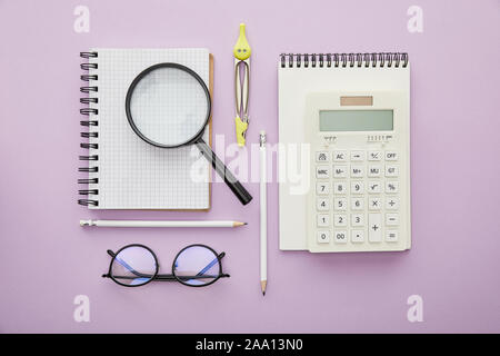 Vista superiore della lente di ingrandimento sul notebook vicino a calcolatrice e vetri isolati su viola Foto Stock