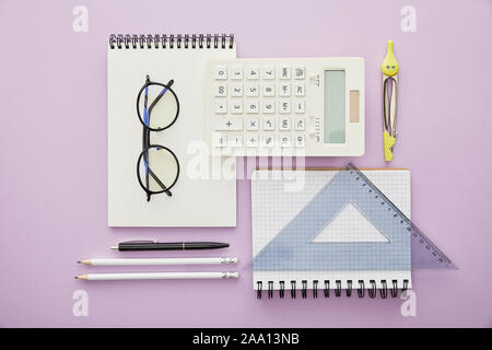 Lay piatto con i righelli e calcolatrice vicino al notebook e articoli di cartoleria isolati su viola Foto Stock