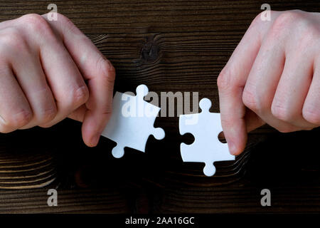 Tenere le mani di due pezzi di un puzzle in bianco su uno sfondo di legno. Close up. Foto Stock