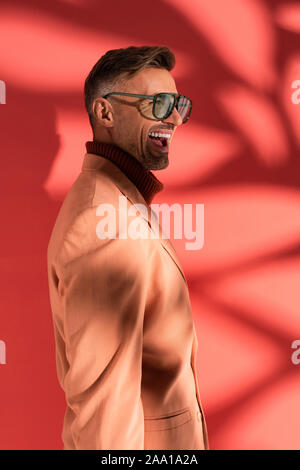 Felice ed elegante uomo in occhiali da sole sul rosso con le ombre Foto Stock