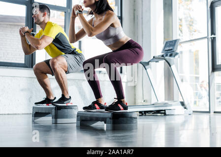 Vista ritagliata della sportivo e sportive facendo squat sul passo di piattaforme nel centro sportivo Foto Stock