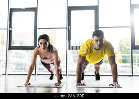 Sportivo e sportive facendo plank su tappetini fitness nel centro sportivo Foto Stock