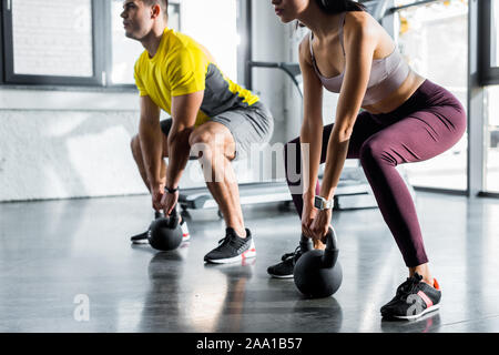 Vista ritagliata della sportivo e sportive facendo squat con pesi nel centro sportivo Foto Stock