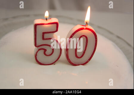 La masterizzazione di rosso e candele bianche che formano il numero cinquanta su una torta decorata con meringa bianca Foto Stock