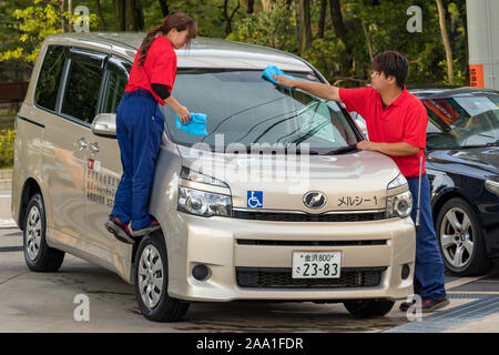 Due maschi e femmine di giapponese stazione gas lavoratori, la pulizia del parabrezza di un cliente in auto a Kanazawa, Giappone. Foto Stock