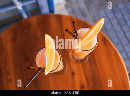 Due cocktail tropicali ornato da succo di arancia e illuminata dal sole al tramonto sul tavolo in legno di un lungomare mediterraneo cafe. Piatto stile di laici. C Foto Stock